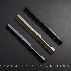 May include: Three metal rulers in black, silver, and blue, with a black and white graphic design on the side. The rulers are arranged in a diagonal pattern on a black surface. The text "TP | REFORM OF THE WRITING TOOL" is at the bottom of the image.