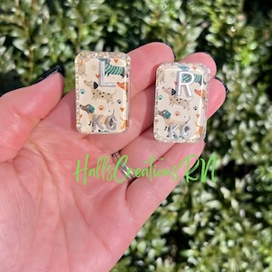May include: Two rectangular, clear resin keychains. Each keychain features a dachshund pattern with the letters "L" and "R" in silver, along with the initials "KG". The background is a cream color with paw prints and hearts.