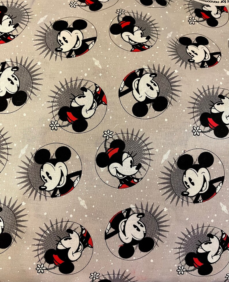 May include: A gray fabric with a repeating pattern of Mickey Mouse in a circle. The background is a light gray with white speckles. Mickey Mouse is wearing red shorts and yellow shoes.