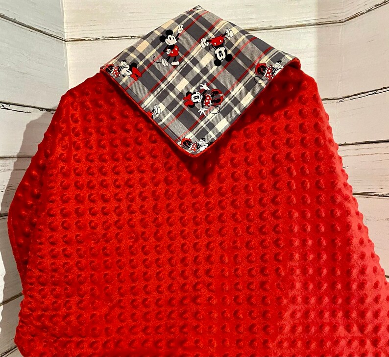 May include: Red minky baby blanket with a plaid fabric panel featuring Mickey Mouse and Minnie Mouse characters. The panel is attached to the blanket with a decorative stitch.