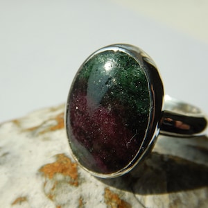 May include: A silver ring featuring an oval green and purple gemstone. The gemstone has a sparkly, textured surface.