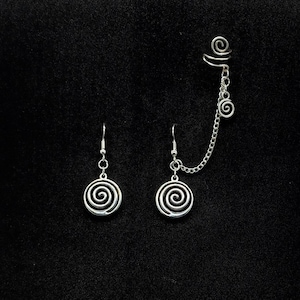 May include: A set of silver earrings and an ear cuff. The earrings and ear cuff have a spiral design. The ear cuff is connected to one earring with a fine chain. The jewellery is shown against a black background.