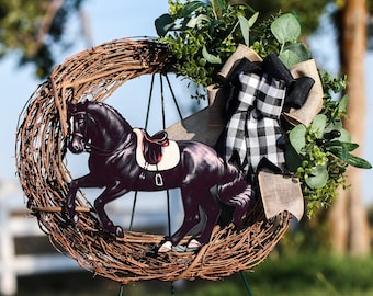 May include: A decorative wreath featuring a dark brown horse cutout with a saddle, set against a woven grapevine base. The wreath is adorned with greenery, a burlap ribbon, and a black and white checkered bow, creating a rustic equestrian theme.