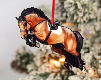 May include: A brown and black horse ornament jumping over a fence. The horse is wearing a saddle and bridle. The ornament is made of wood and is painted in a realistic style.