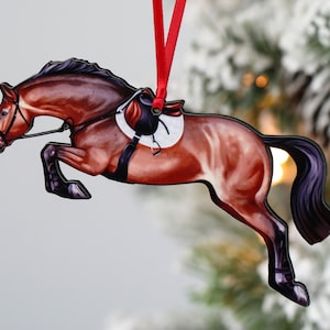 May include: A brown horse ornament with a black saddle and bridle, jumping over an obstacle. The ornament is made of wood and is painted in a realistic style. It is a great gift for horse lovers.