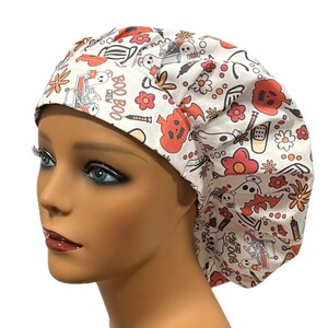 Op de afbeelding: Witte scrub-muts met een Halloween-print met geesten, pompoenen, vleermuizen en de tekst "Boo Boo Crew".