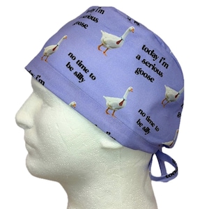 May include: A light purple surgical scrub cap featuring a repeating pattern of white geese with orange beaks and feet. The cap has the phrases "today I'm a serious goose" and "no time to be silly" printed on it.