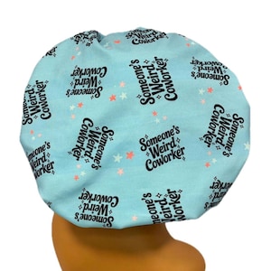 May include: A light blue bouffant cap with the text "Someone's Weird Coworker" in black script, interspersed with small orange and white stars. The cap is designed to cover the hair.