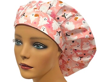 May include: A pink and white Halloween bouffant scrub hat featuring a repeating pattern of friendly ghosts, jack-o'-lanterns, stars, and the word "Boo!" The hat is designed to cover the hair and is likely for medical or culinary use.