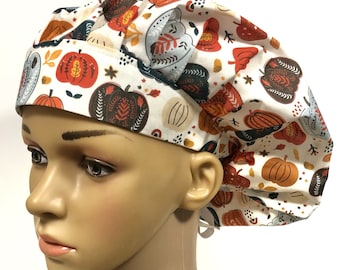 May include: A white scrub hat with a fall-themed print featuring orange, brown, and green pumpkins, leaves, and stars.