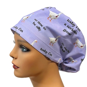 May include: A light purple scrub cap featuring white geese and the phrases "today I'm a serious goose" and "no time to be silly" in black text. The cap is designed to cover the head and hair.