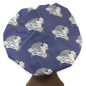 May include: A blue shower cap with a repeating pattern of possums with the text "You should smile more" on a banner. The possums are white and gray with pink flowers.