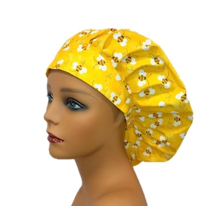 May include: Yellow bouffant scrub cap with a repeating pattern of cartoon bees. The cap is made of a lightweight fabric and is designed to cover the hair. The background is white.