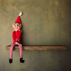 May include: A red and white striped elf doll sitting on a wooden shelf against a green background.