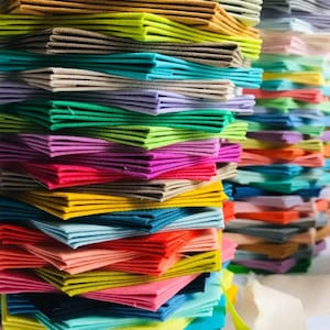 May include: A stack of colourful fabric squares, folded and arranged in a rainbow pattern. The fabric is a variety of textures and colours, including yellow, green, blue, red, pink, and purple.