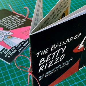 The Ballad of Betty Rizzo, an Abortion Story by Rachelle Meyer, front and back cover on a cutting mat