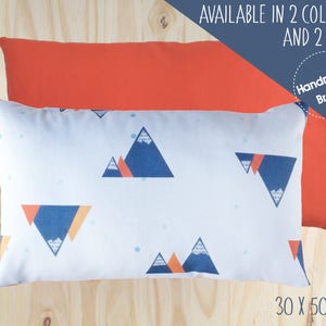 Può includere: Due cuscini decorativi, uno rosso e uno bianco con un motivo geometrico a forma di montagna in blu, arancione e bianco. Il cuscino bianco ha il testo "Handmade Brand" e "Available in 2 colours and 2 sizes". I cuscini misurano 30 x 50 cm.