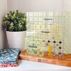 May include: A set of three yellow and white Omnigrid quilting rulers on a wooden base with the text "Timber Notions".
