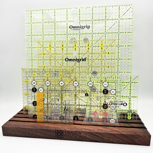 May include: A set of four clear yellow Omnigrid rulers with black markings, displayed on a dark brown wooden stand. The stand has the words "Timber Notions" engraved on the front.