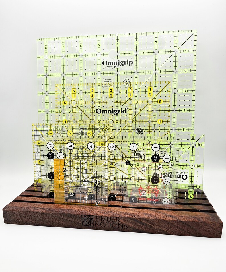 May include: A set of four clear yellow Omnigrid rulers with black markings, displayed on a dark brown wooden stand. The stand has the words "Timber Notions" engraved on the front.
