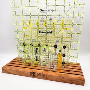 May include: A wooden ruler stand with a yellow and black Omnigrid ruler. The stand is made of cherry wood and has the words "Timber Notions" engraved on the front.