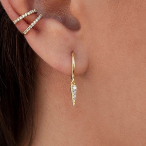 Könnte beinhalten: Nahaufnahme eines Ohrs mit drei goldenen Ohrringen. Die Ohrringe sind eine kleine Stange mit drei Diamanten, ein doppelter Ring mit Diamanten und ein Ring mit einer diamantbesetzten Spitze.