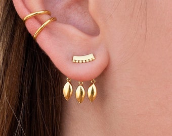 May include: Gold ear cuff and earrings with a leaf design. The ear cuff is a double hoop and the earrings have three small leaves dangling from a curved bar.