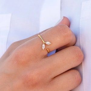 Op de afbeelding: Een gouden ring met twee kleine diamantvormige stenen die in de band zijn gezet. De ring wordt gedragen aan de wijsvinger van een hand.