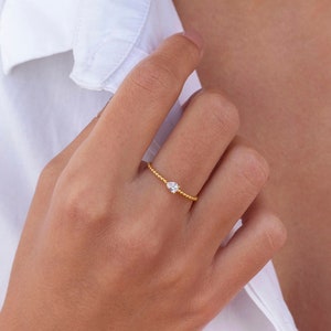 Puede incluir: Un delicado anillo de oro con una sola piedra pequeña y clara engastada en el centro.