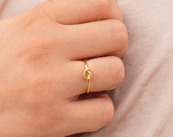 May include: A gold knot ring on a finger. The ring is simple and delicate, with a smooth finish.