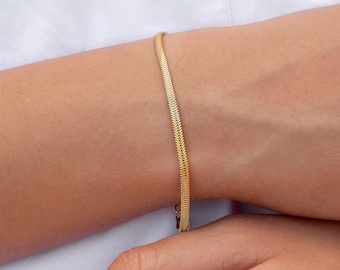 Könnte beinhalten: Ein goldenes Kettenarmband mit einem zarten, schlangenartigen Design.