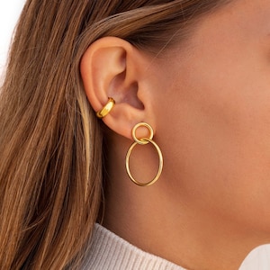 Pode incluir: Brincos de argola de ouro com uma argola menor dentro da argola maior. Os brincos são usados por uma pessoa com cabelo castanho e comprido.
