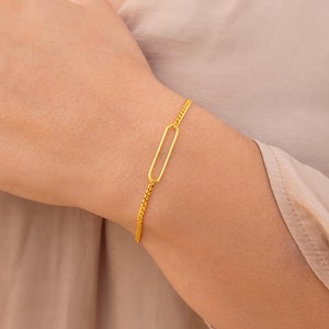 Puede incluir: Un brazalete de cadena dorada con un simple dije de forma ovalada.