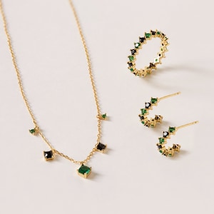 May include: A gold necklace with a green and black square pendant and matching earrings. The necklace has a delicate chain with small green and black square accents.