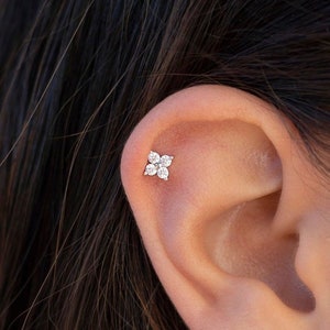 Puede incluir: Primer plano de una oreja con un peque&ntilde;o pendiente de plata con forma de flor con cinco piedras preciosas transparentes.