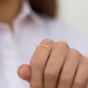 Può includere: Un anello d'oro a forma di orecchie di gatto. L'anello è sottile e delicato, con piccole orecchie di gatto sulla parte superiore.