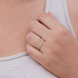 May include: A close-up of a hand wearing three gold beaded rings.