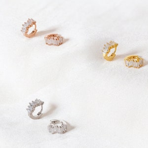 K&ouml;nnte beinhalten: F&uuml;nf Paar Creolen mit einer Reihe von baguettef&ouml;rmigen Zirkonia-Steinen. Die Ohrringe sind in Silber, Gold und Ros&eacute;gold erh&auml;ltlich.
