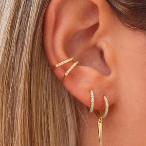 May include: Gold earrings with small sparkling stones. The earrings are a hoop style with a dangling spike.