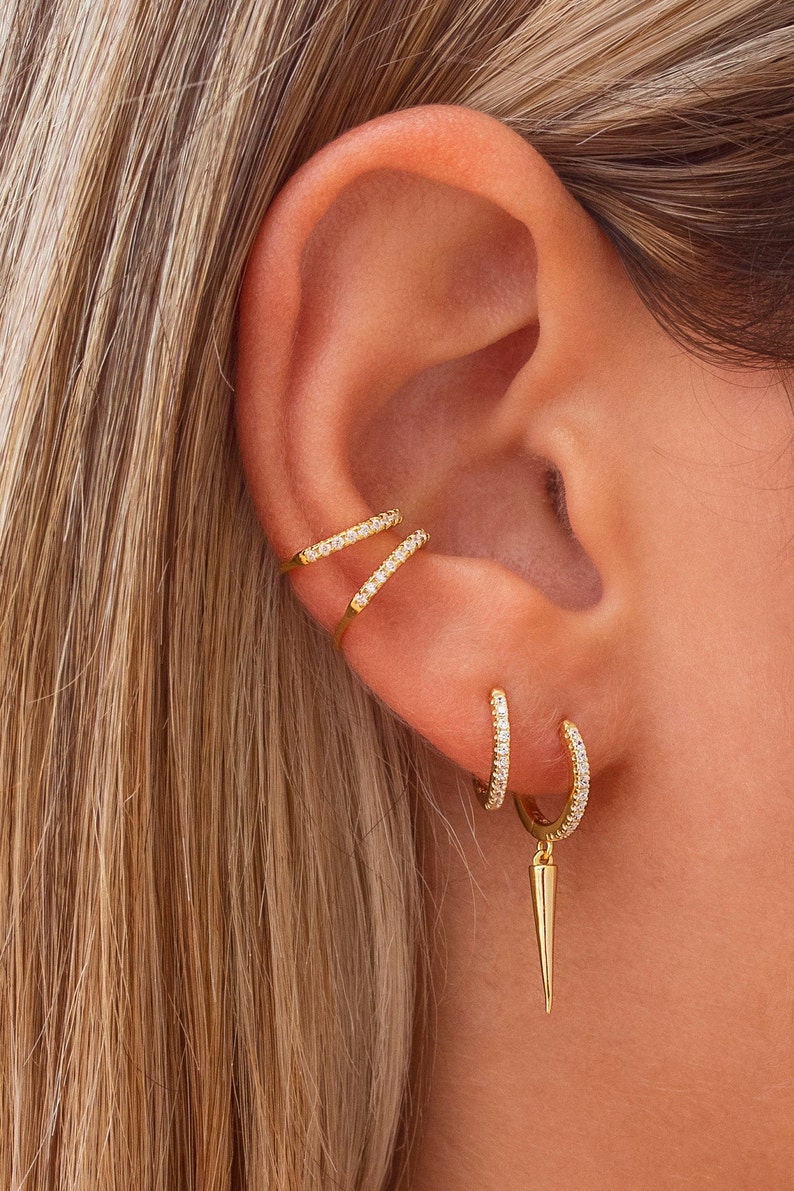 May include: Gold earrings with small sparkling stones. The earrings are a hoop style with a dangling spike.