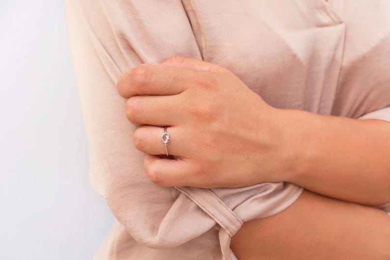 Puede incluir: Un anillo de plata con un dise&ntilde;o de nudo en el dedo de una persona.