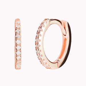 May include: A pair of rose gold hoop earrings with a single row of clear cubic zirconia stones around the edge.