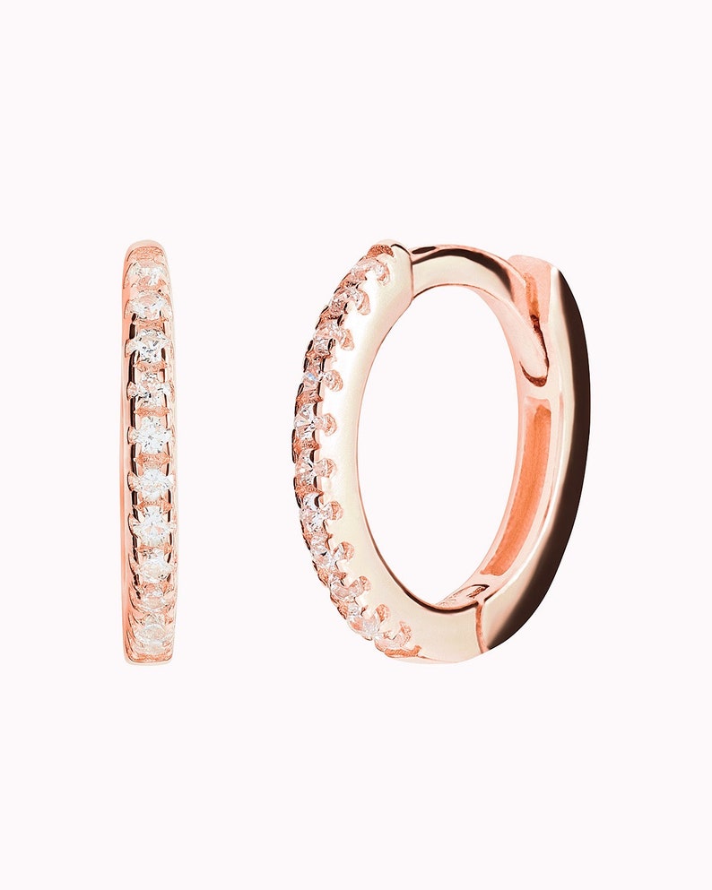 May include: A pair of rose gold hoop earrings with a single row of clear cubic zirconia stones around the edge.