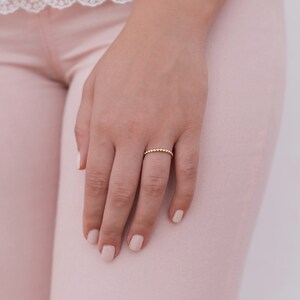 May include: A delicate gold ring with a beaded design. The ring is worn on the ring finger of a hand.