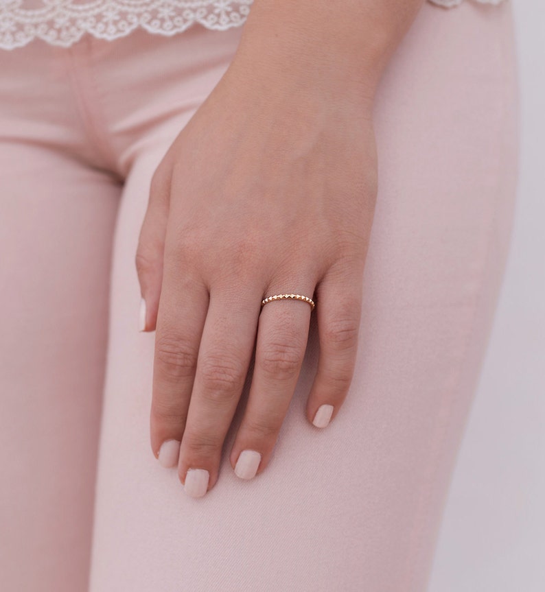 May include: A delicate gold ring with a beaded design. The ring is worn on the ring finger of a hand.