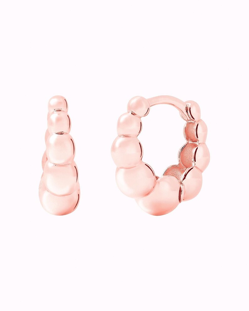 Pu&ograve; includere: Un paio di orecchini a cerchio in oro rosa con un design a perline. Gli orecchini sono realizzati con piccole perline rotonde che sono collegate tra loro per formare una forma a cerchio.