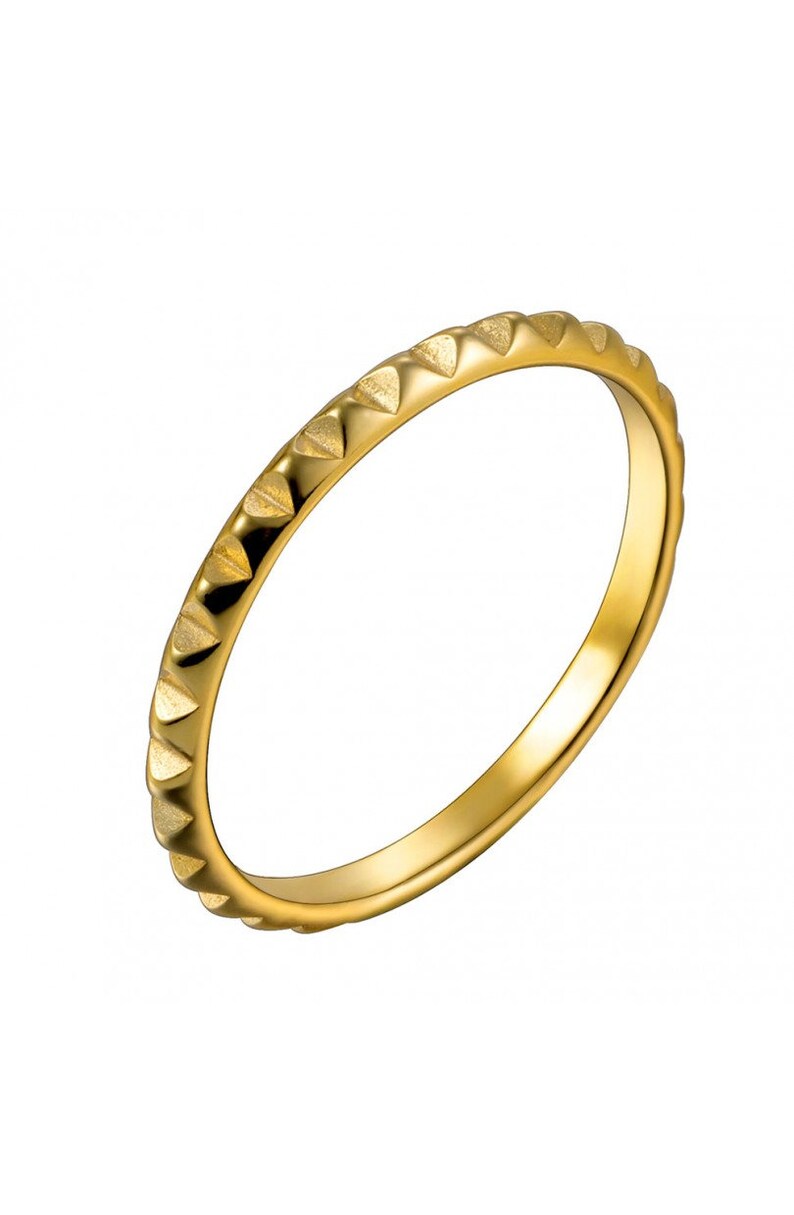 May include: A gold-coloured ring with a textured band. The band is decorated with a series of small, triangular shapes.