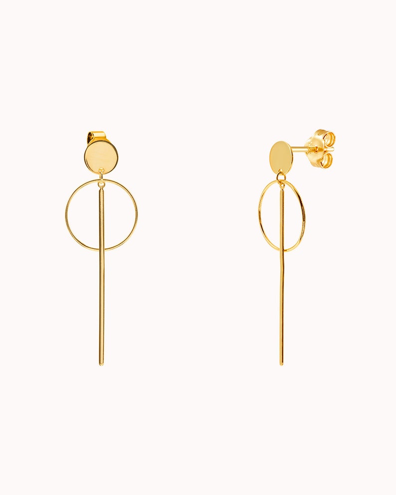 May include: A pair of gold-toned earrings with a circle and a long, thin bar hanging from a small round disc.