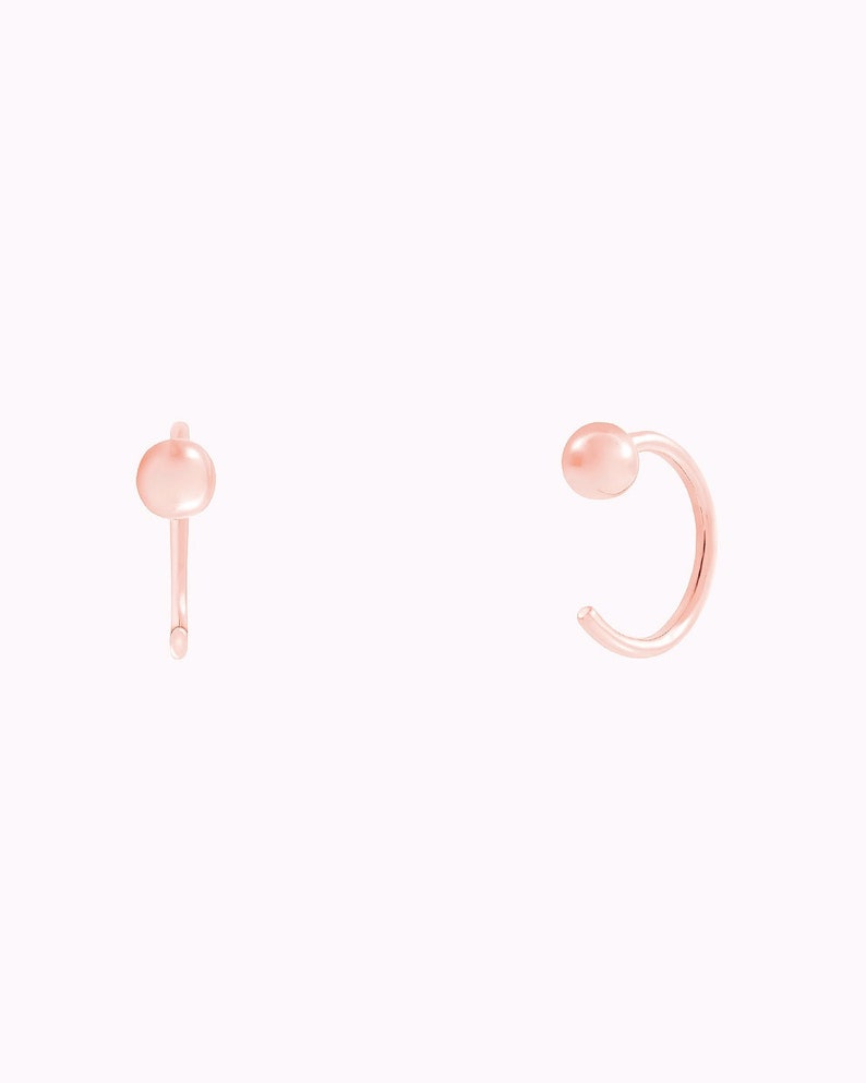 Puede incluir: Un par de pendientes de aro de oro rosa con una peque&ntilde;a bola al final de cada aro.