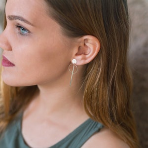 May include: A woman with long brown hair wearing a green tank top and silver earrings with a circle and a long, thin bar.